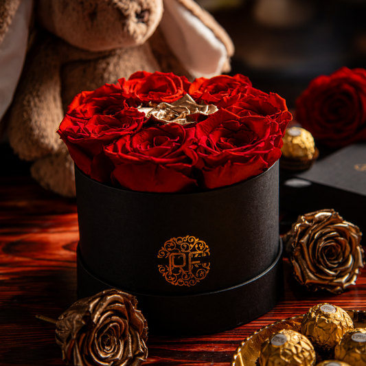Arreglo floral de 8 rosas rojas preservadas con rosa central dorada en estuche cilíndrico de lujo