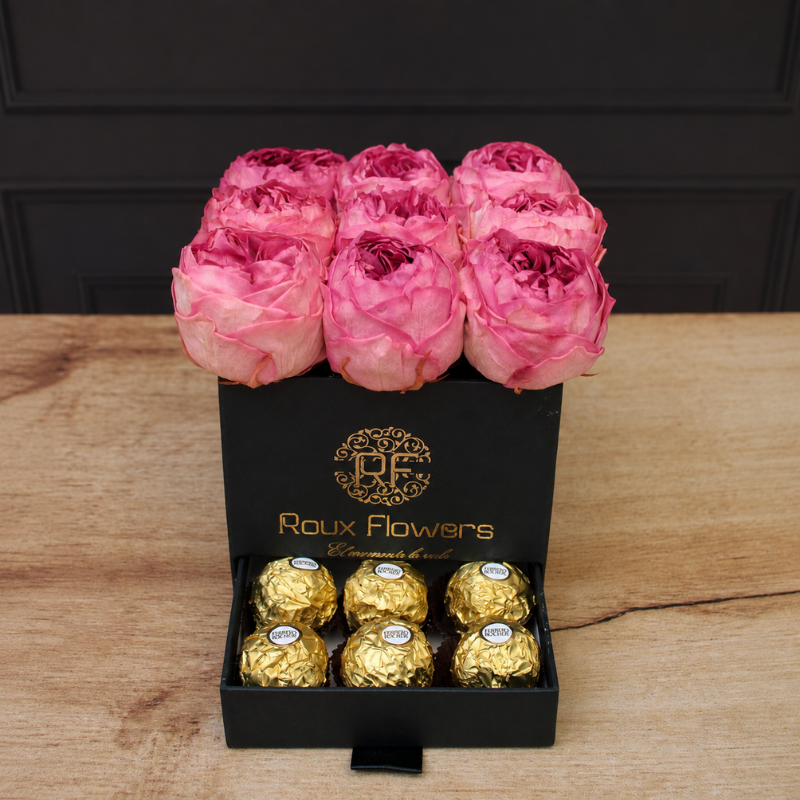 Caja negra de lujo con 9 peonías preservadas rosa intenso y cajón con chocolates Ferrero Rocher sobre madera