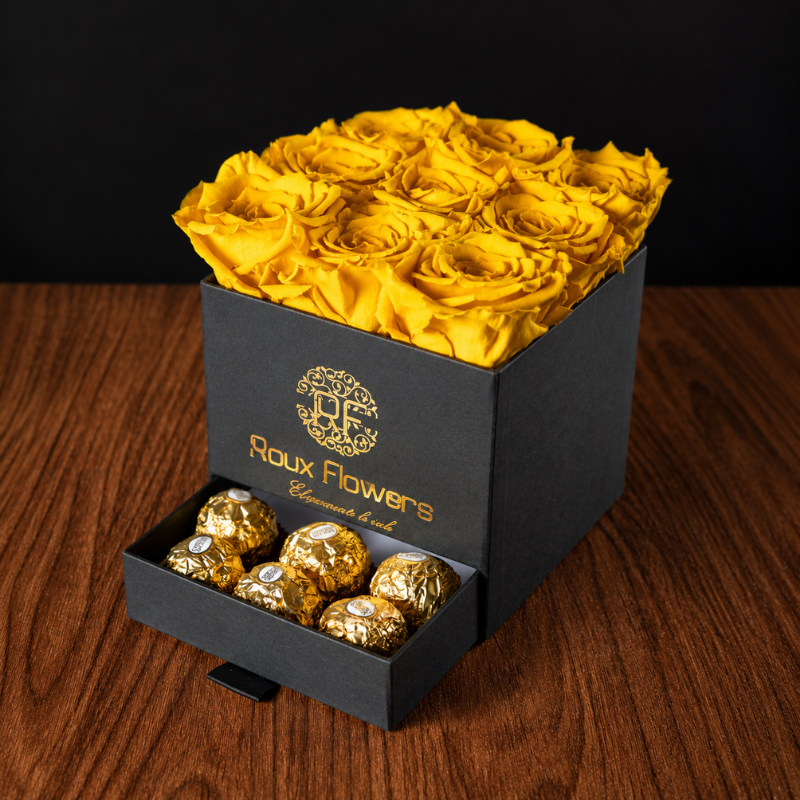 Caja de regalo negra con 9 rosas preservadas amarillas y cajón con chocolates Ferrero Rocher sobre mesa de madera