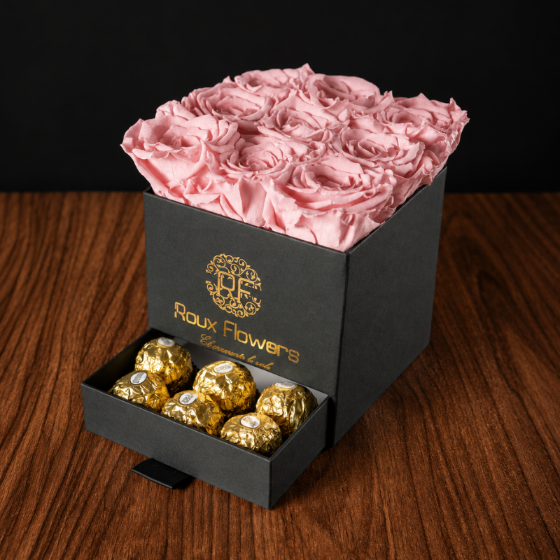 Caja cuadrada negra con rosas preservadas en tono rosa claro y chocolates de regalo
