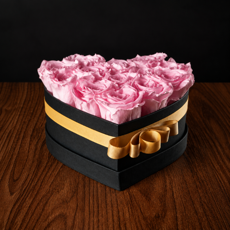 Caja en forma de corazón con rosas naturales preservadas en color rosa claro y lazo dorado para regalo